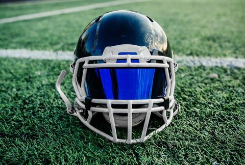 Football helmet with a visor atop a grassy football field Football helmet with a visor atop a grassy football field